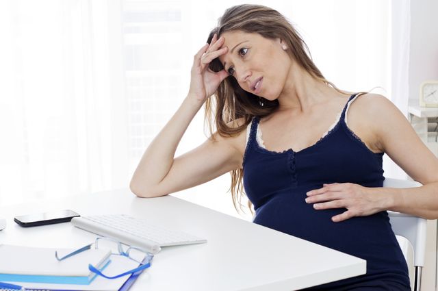 A pregnant woman sitting at a computer desk at home and looking stressed out